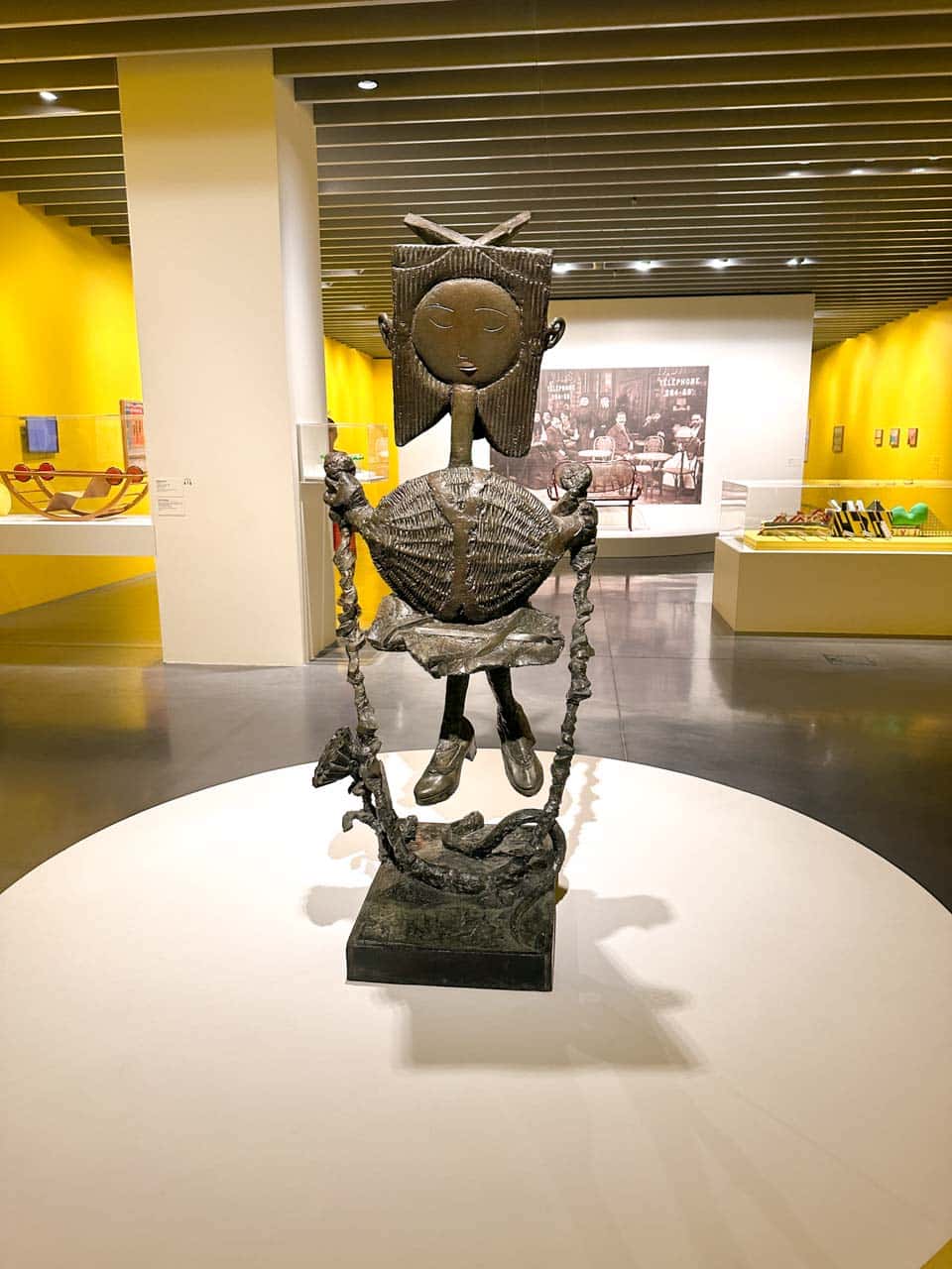 A metal sculpture of a woman with long arms, holding two large chain links, displayed at Centre Pompidou Malaga