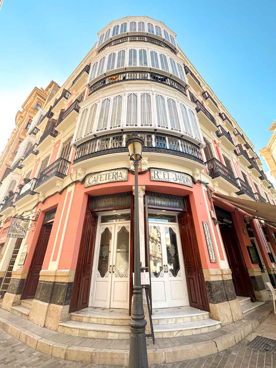 A street view of a curved building with white balconies, red and cream walls, and a 'Cafeteria' sign