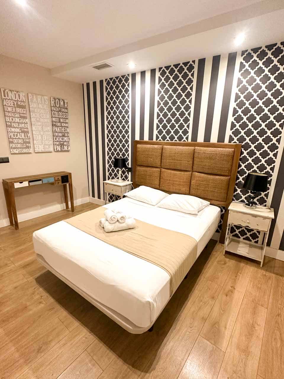 A modern bedroom with black and white patterned walls, a double bed with tan bedding, and two white towels on top