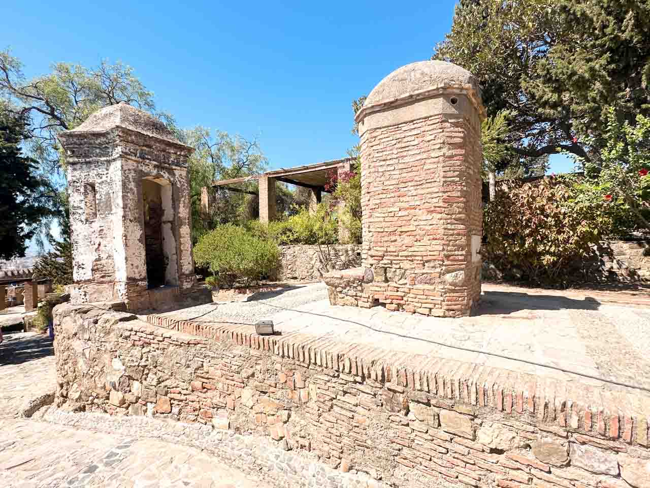 Watchtowers with domed tops, connected by a wall, amongst greenery inside the Gibralfaro Castle in Malaga, Spain