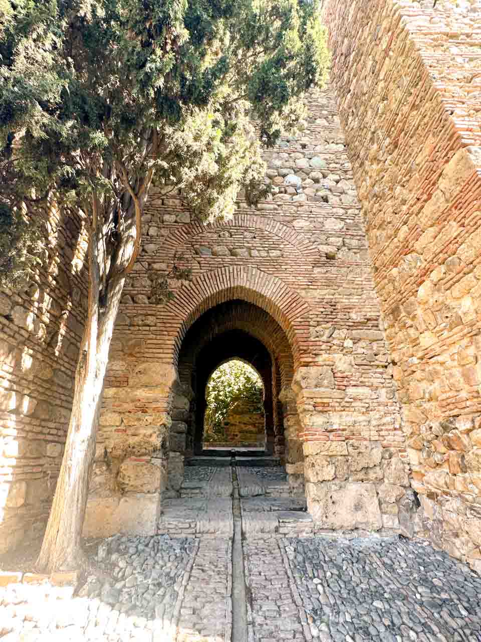 A cobblestone path leading through archways in a brick wall inside the Alcazaba of Malaga