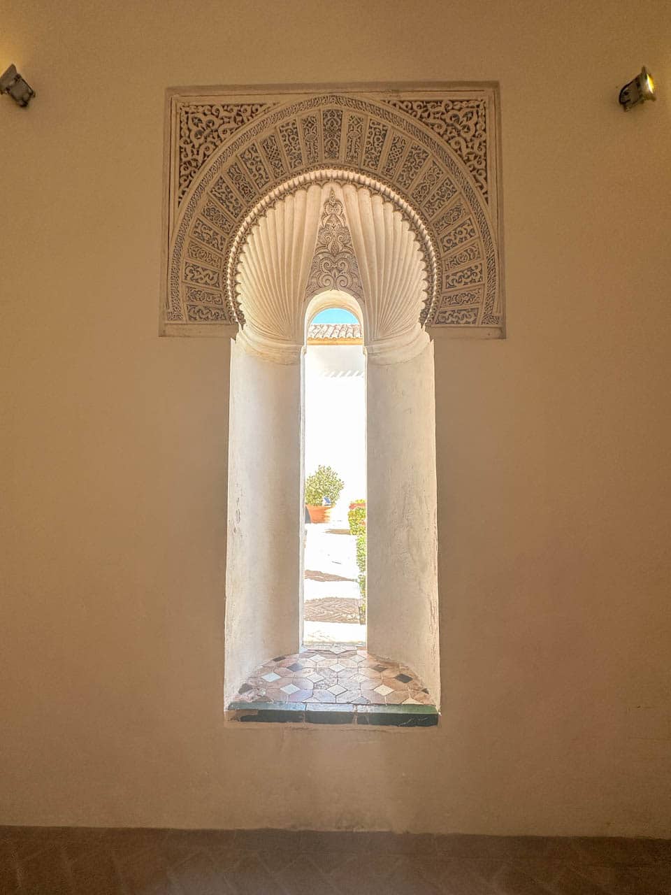 An ornate arched window with intricate carvings overlooking a courtyard at the Alcazaba of Malaga