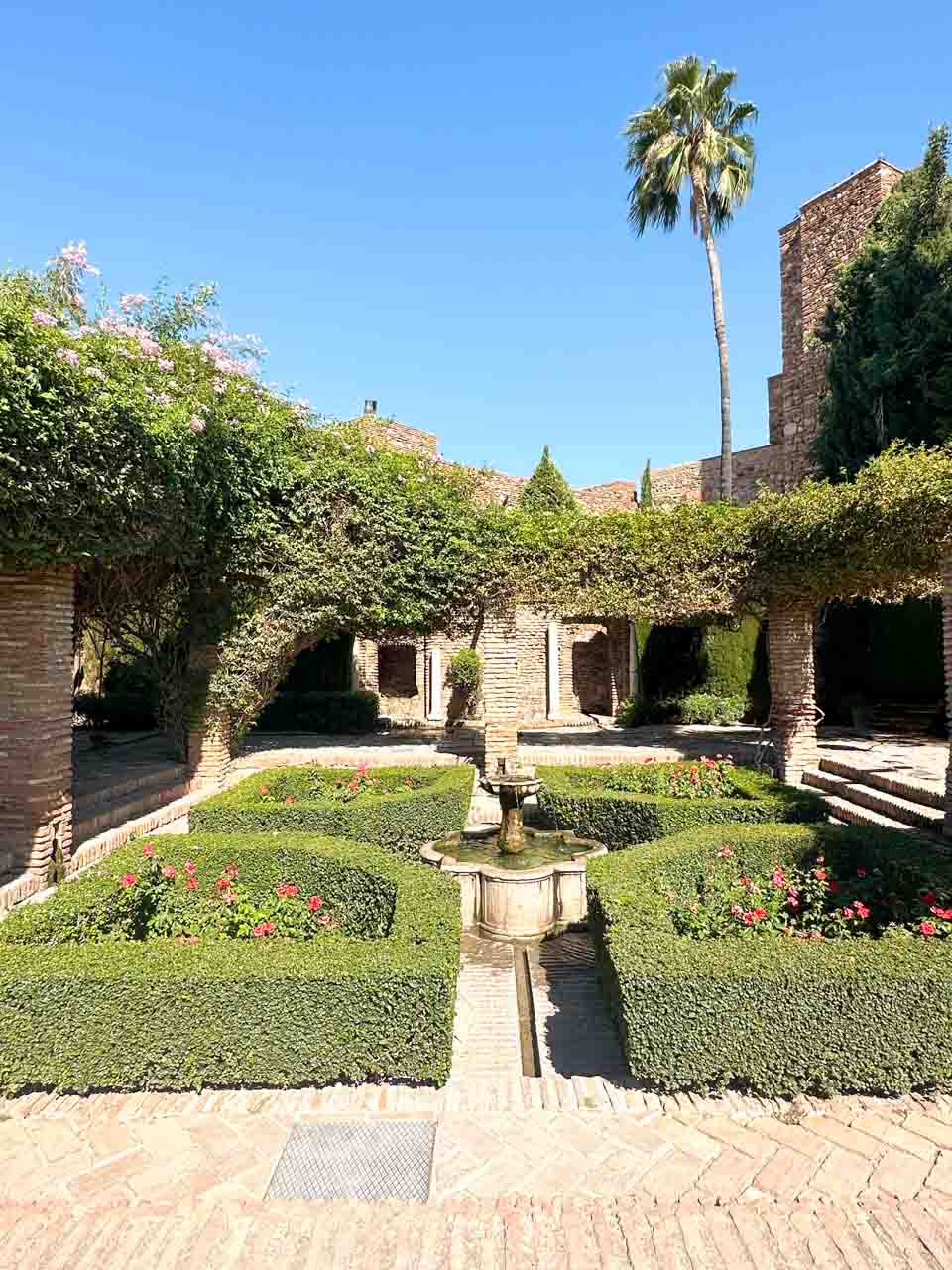 A lush garden with geometrical hedge designs and a central fountain at the Alcazaba of Malaga