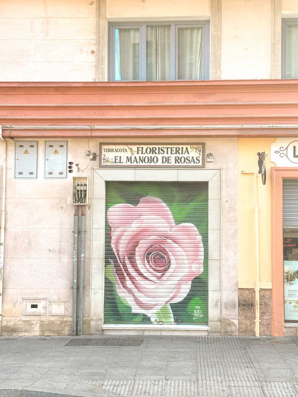 A shopfront in Malaga with a large painted rose on the shutter, titled "Floristeria El Manojo de Rosas"