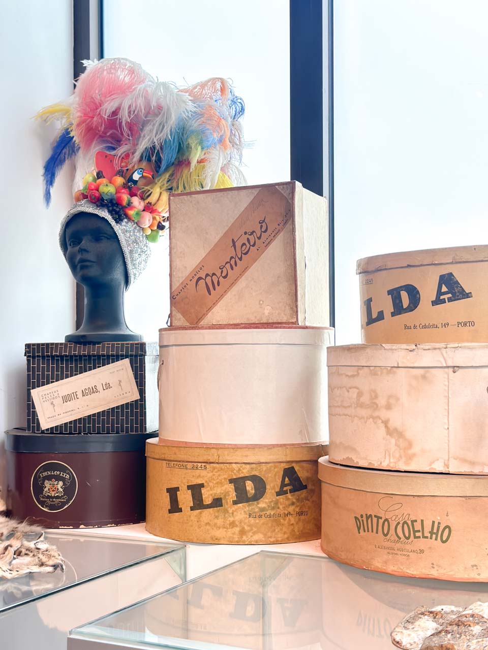 Vintage hat boxes stacked on a shelf beside a mannequin head wearing a colourful feathered headdress at the Automobile and Fashion Museum in Malaga, Spain