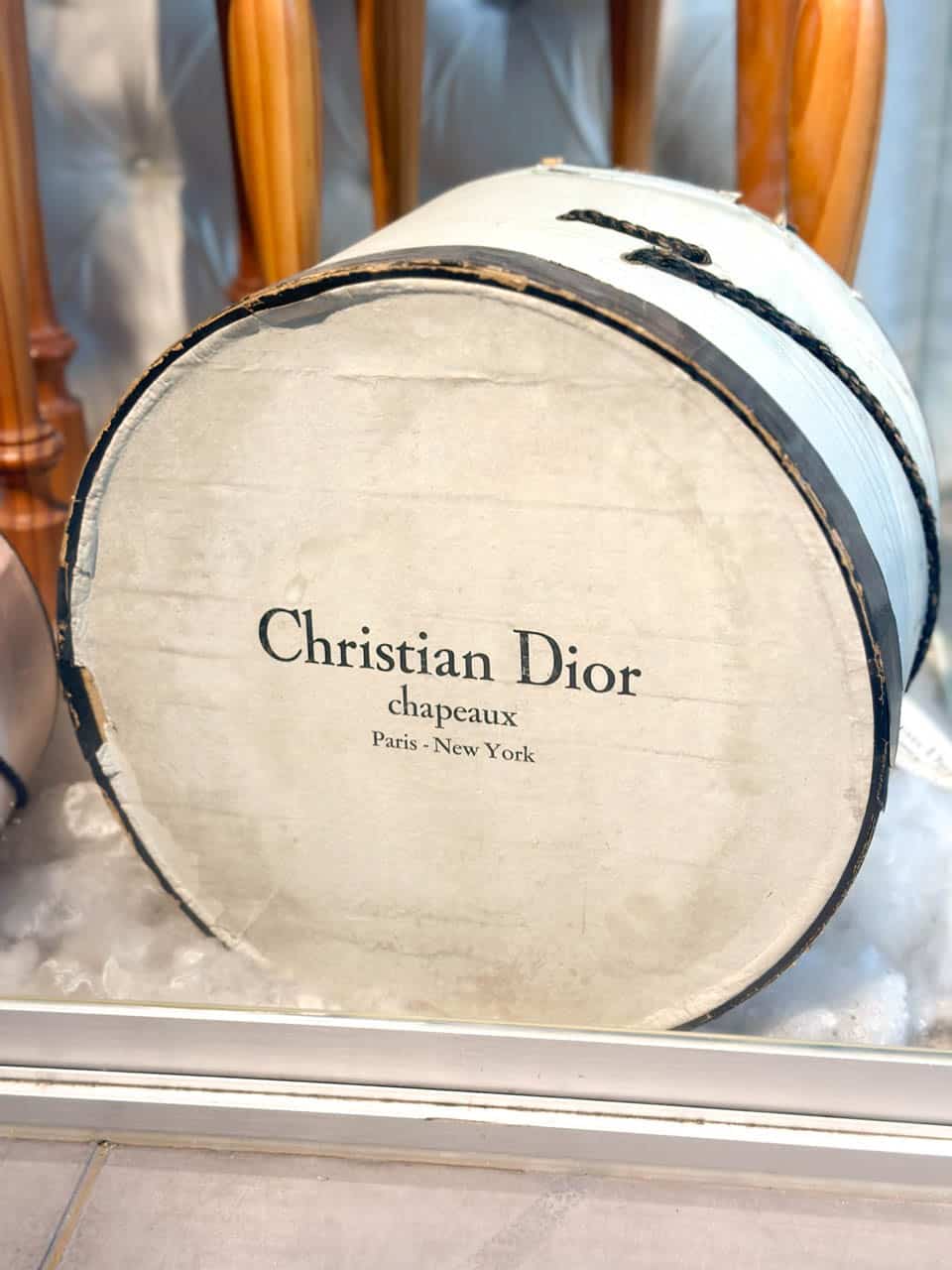 An antique Christian Dior hat box, round and white with black trim, against a padded display background at the Automobile and Fashion Museum in Malaga, Spain