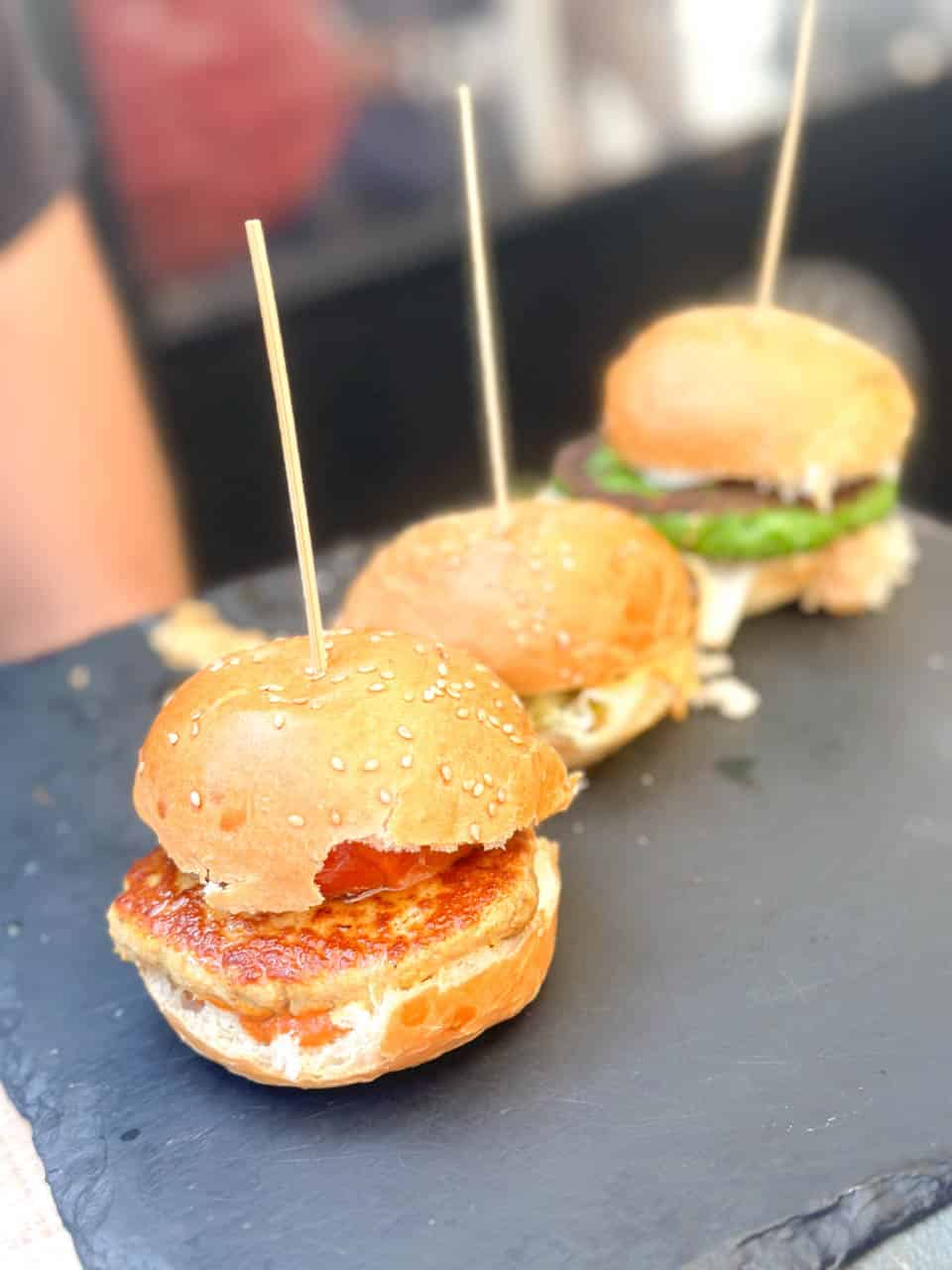 Three mini burgers with sticks through them on a slate tray