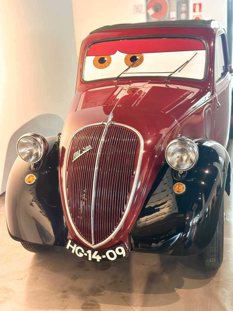 A vintage car in burgundy with large eyes on the windscreen at the Automobile and Fashion Museum in Malaga, Spain