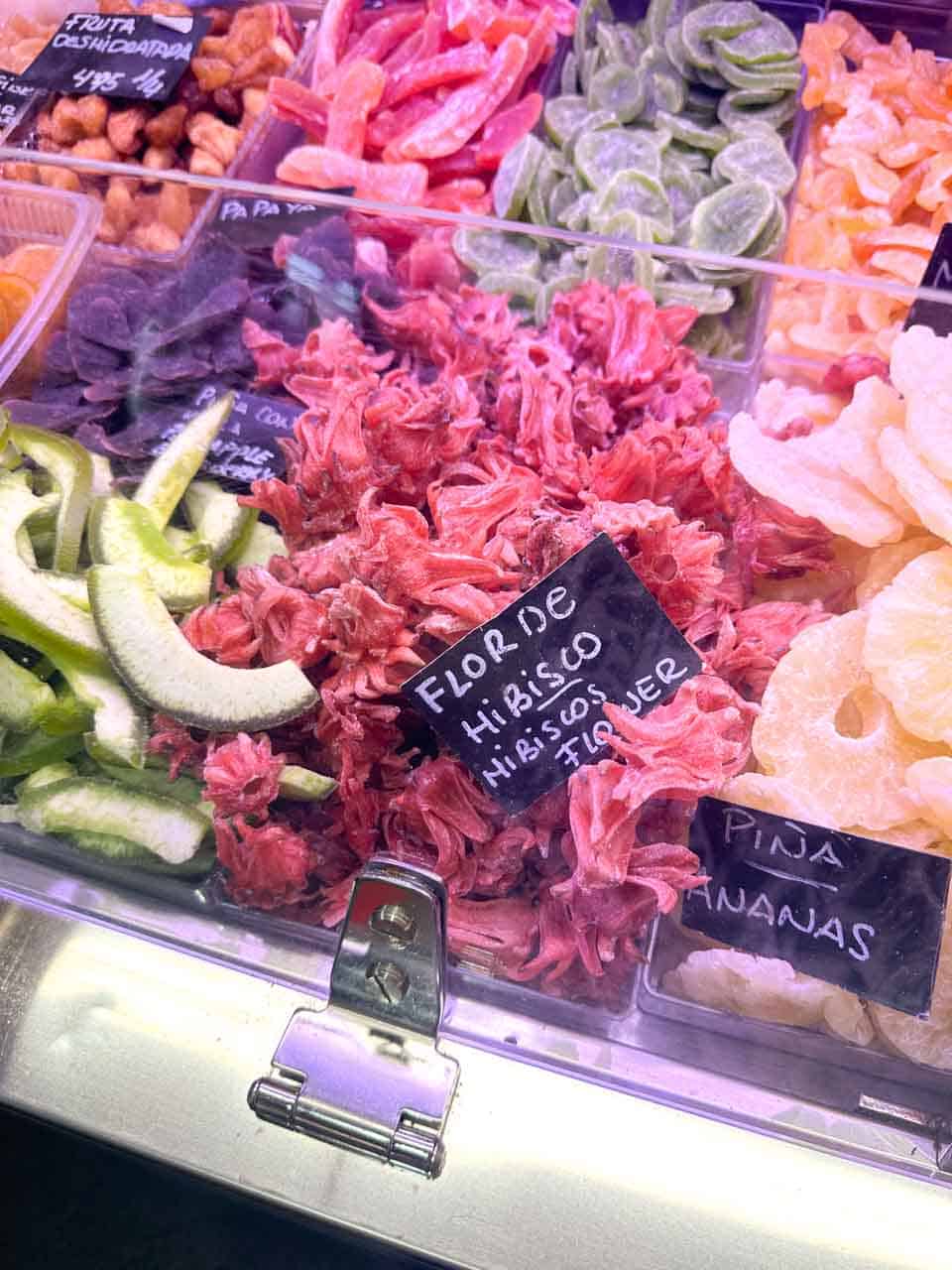 Dried hibiscus flowers among a variety of candied fruits, presented in a market stall at the Atarazanas Market in Malaga, Spain