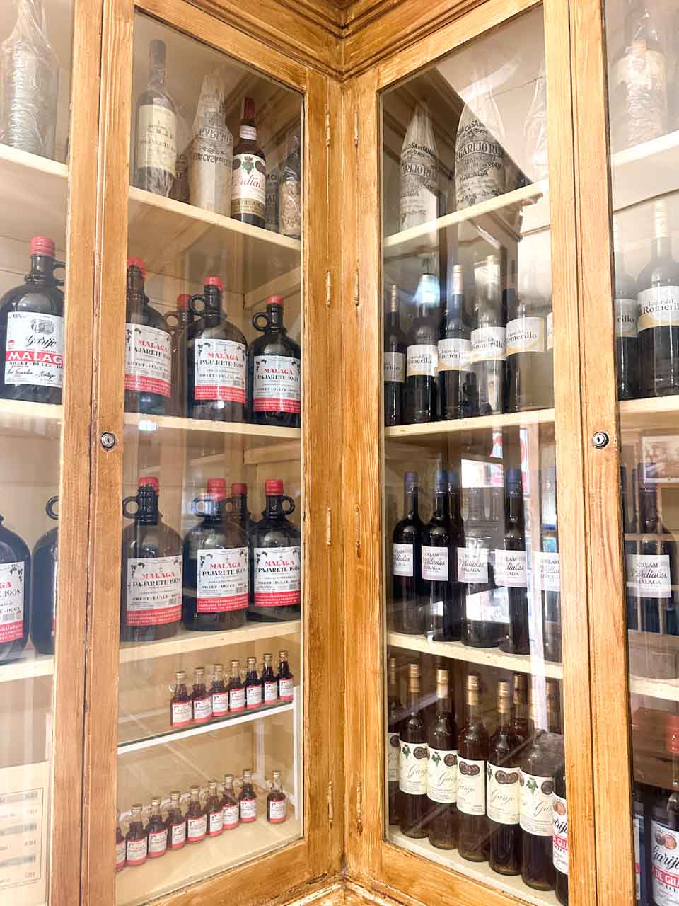 A wooden cabinet displaying an array of traditional Malaga wines and liquors at Antigua Casa de Guardia