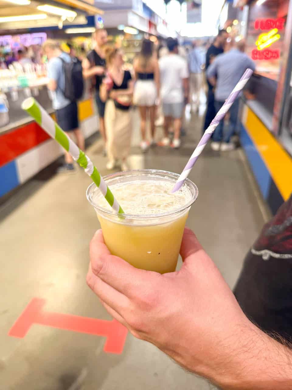 A man holding a plastic cup with sugarcane juice and a striped straw inside the Mercado Central de Atarazanas &ndash; Great Market Hall in Malaga