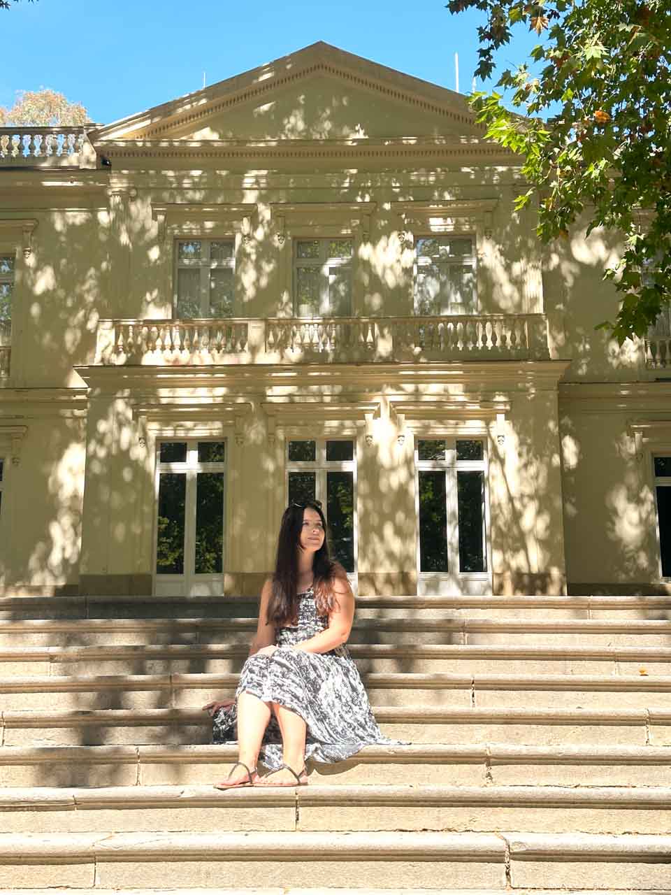 A woman sitting on the steps of a large, cream-coloured house inside Malaga's botanical gardens
