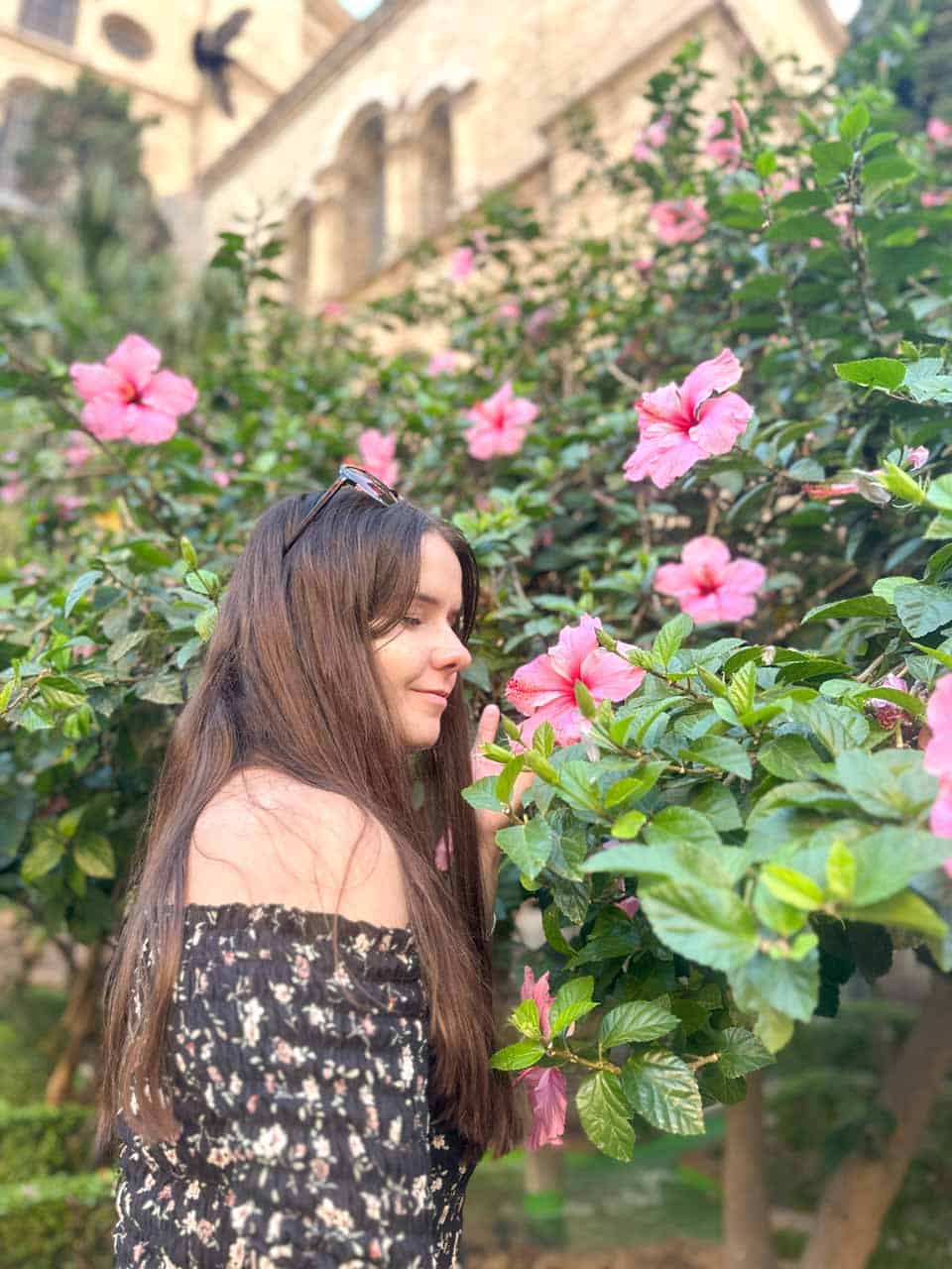A woman smelling pink flowers, with Malaga Cathedral in the background