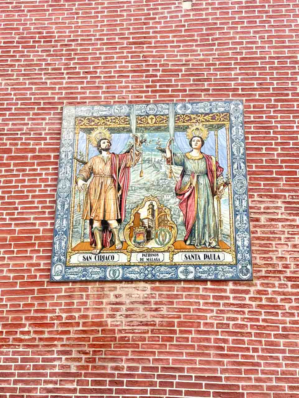 A ceramic tile mural depicting two figures of Spanish saints on a brick wall