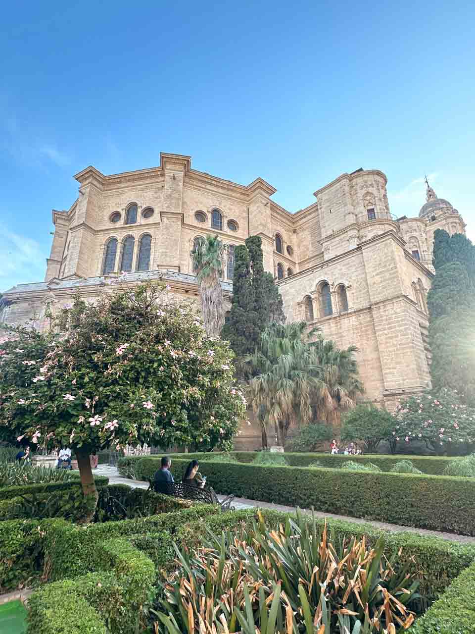 Malaga Cathedral overlooking a lush garden, with a vintage street lamp in the foreground