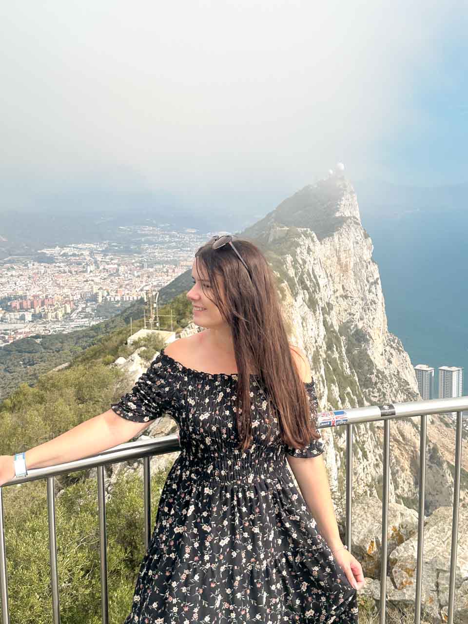 A young woman in a floral dress standing on a viewing platform overlooking the sharp, rocky edge of Gibraltar Rock