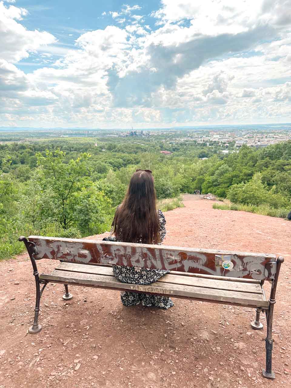 Woman sitting on a bench on top of Halda Ema (Ema Heap) overlooking a panoramic view of Ostrava