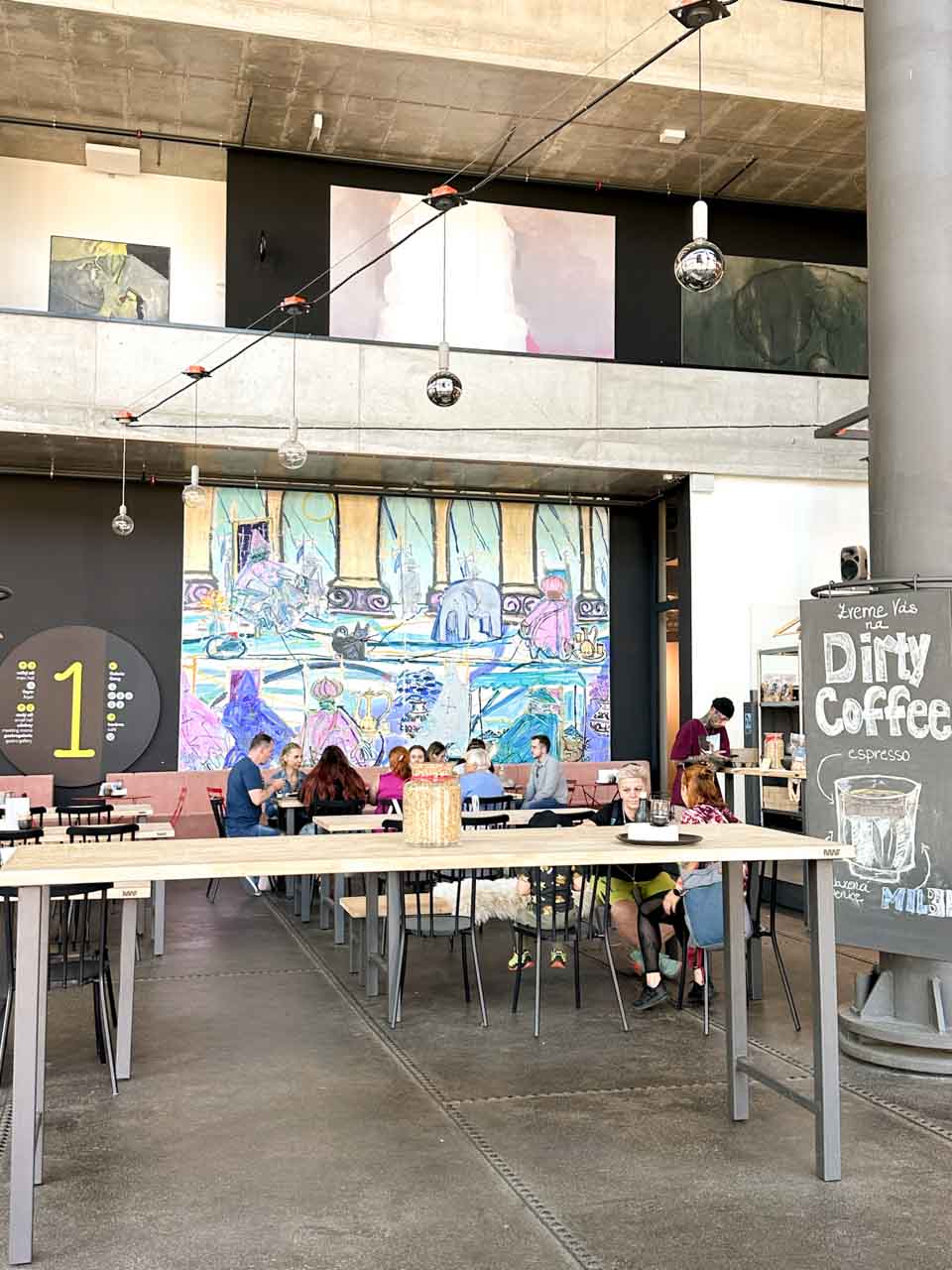Spacious cafe with communal tables and a large mural in the Dolní Vítkovice complex