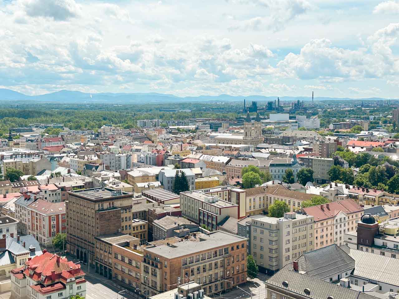 Wide view of Ostrava with buildings, green areas, and mountains in the distance