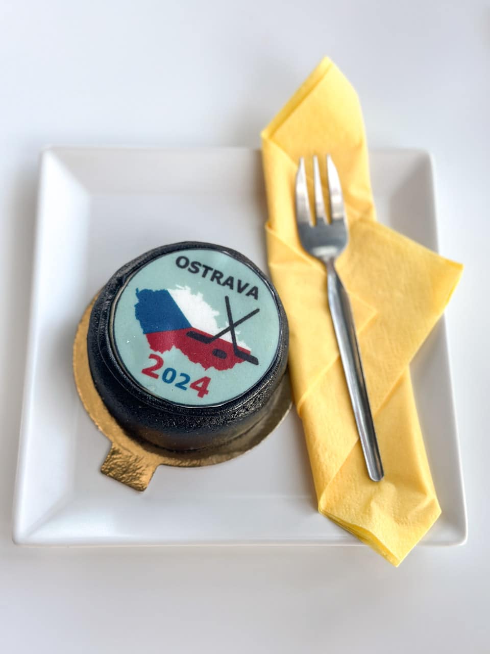 Decorative dessert shaped like a hockey puck with an 'Ostrava 2024' design on a white plate