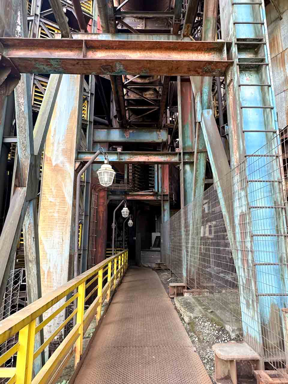 Narrow walkway between aged industrial machinery inside the Bolt Tower in Ostrava