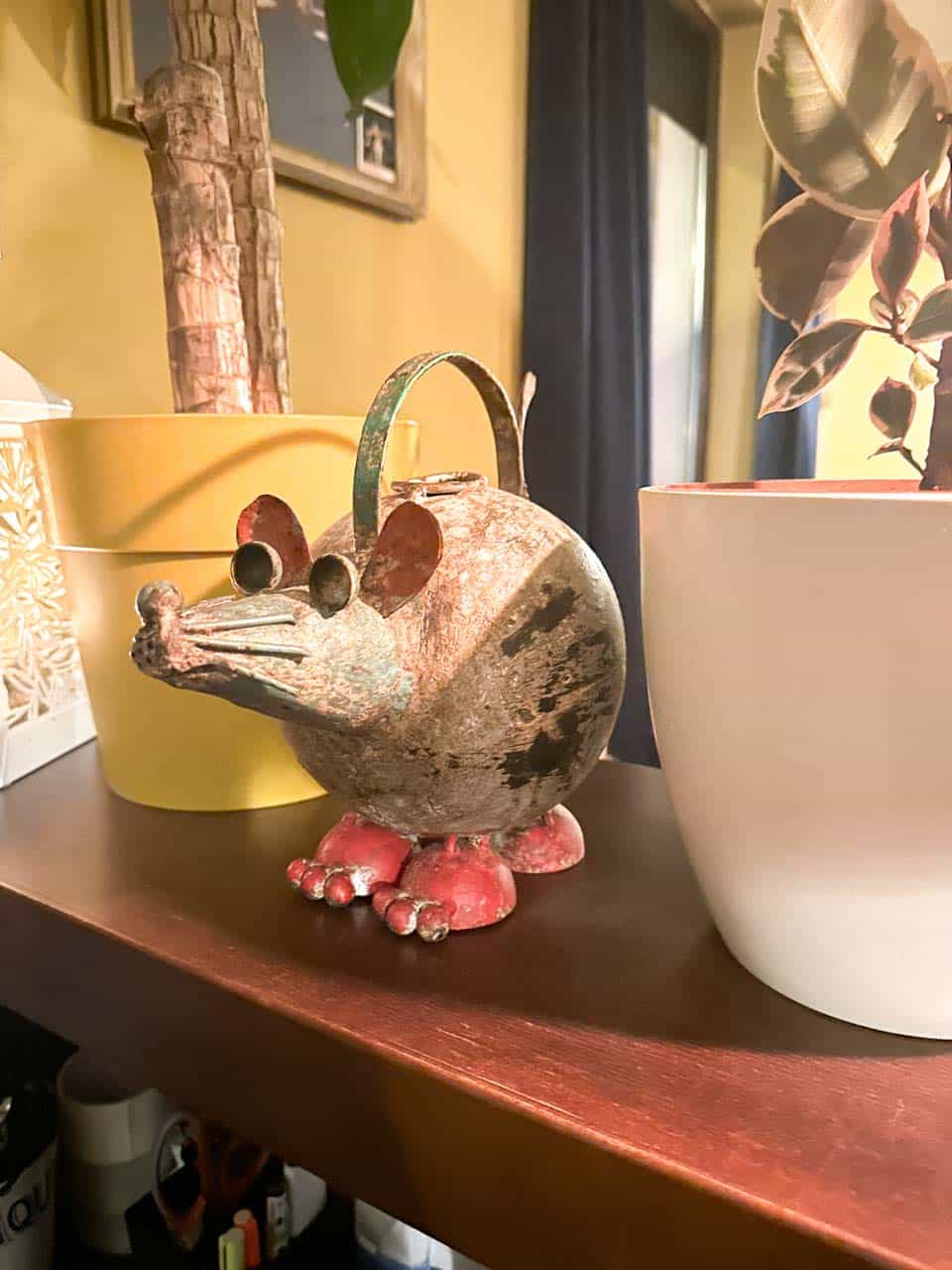 Rustic metal mouse sculpture beside potted plants on a shelf at the Modrá myš cocktail bar in Ostrava
