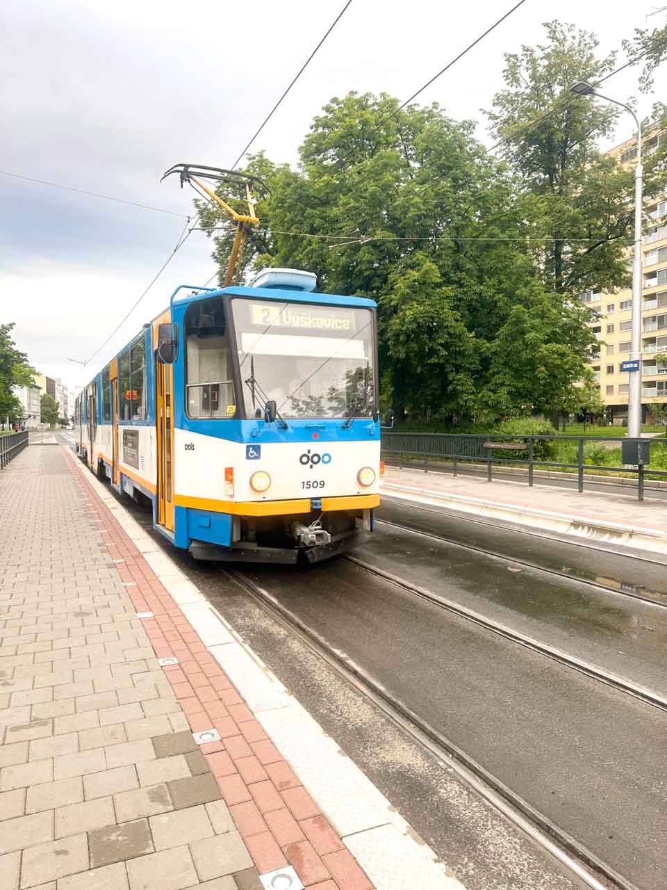 Blue tram arriving at a stop on a cloudy day