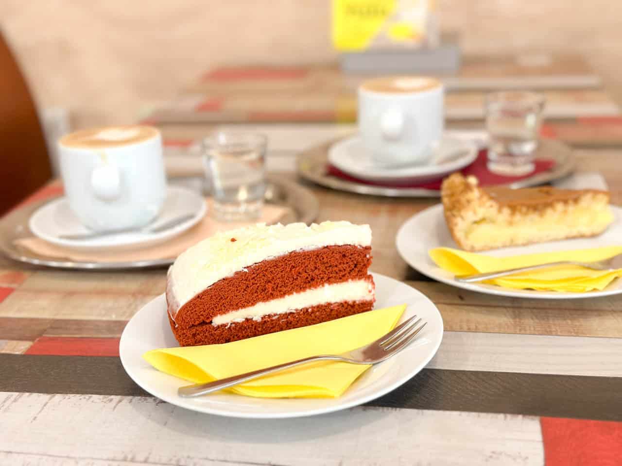 Two cups of coffee, a slice of red velvet cake, and an apple pie with caramel on a cafe table inside Čauky Mňauky Cafe in Ostrava