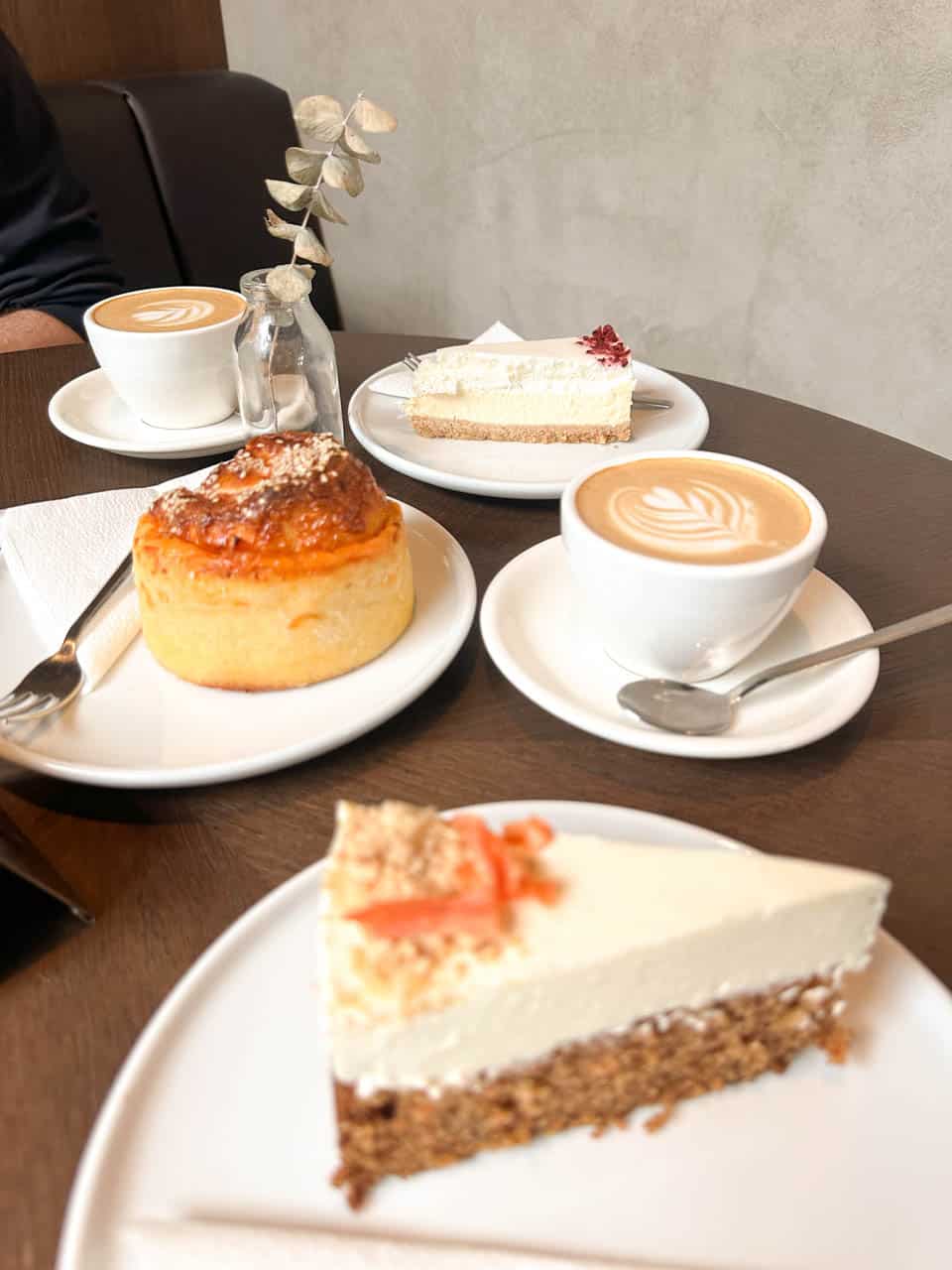 Table with two coffees, a slice of cheesecake, a slice of carrot cake, and a savoury bun at Cokafe in Ostrava