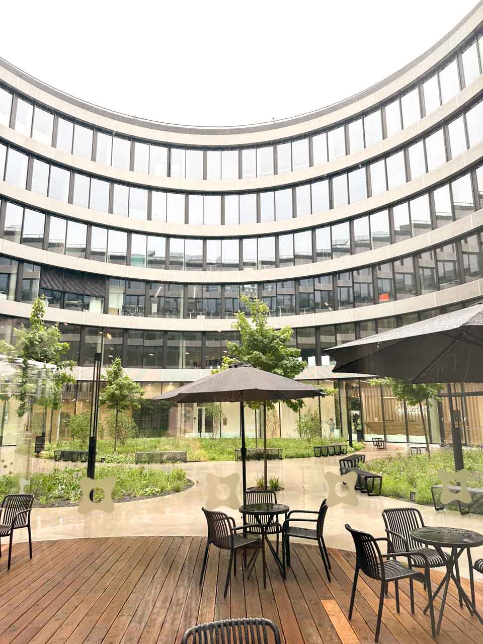 Modern curved building surrounding a courtyard with tables and umbrellas