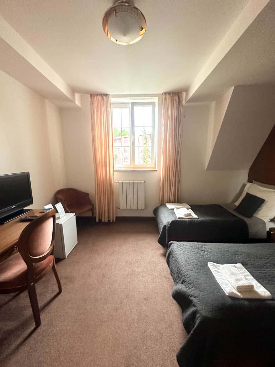 Hotel room with twin beds, desk, and TV under a small window at Retro Hotel Villa Ostrava