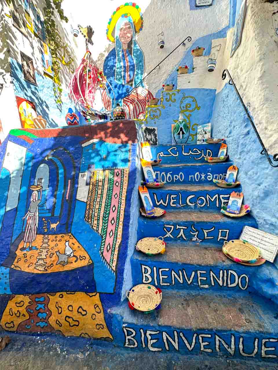 A colourful staircase painted with murals and "Welcome" in several languages, adorned with small woven baskets
