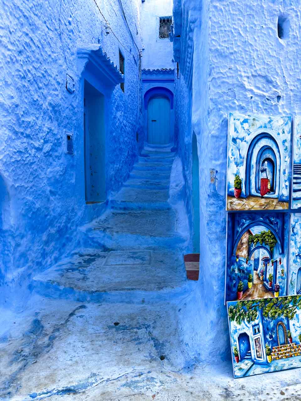 A narrow blue alley with colourful paintings leaning against the wall near the entrance