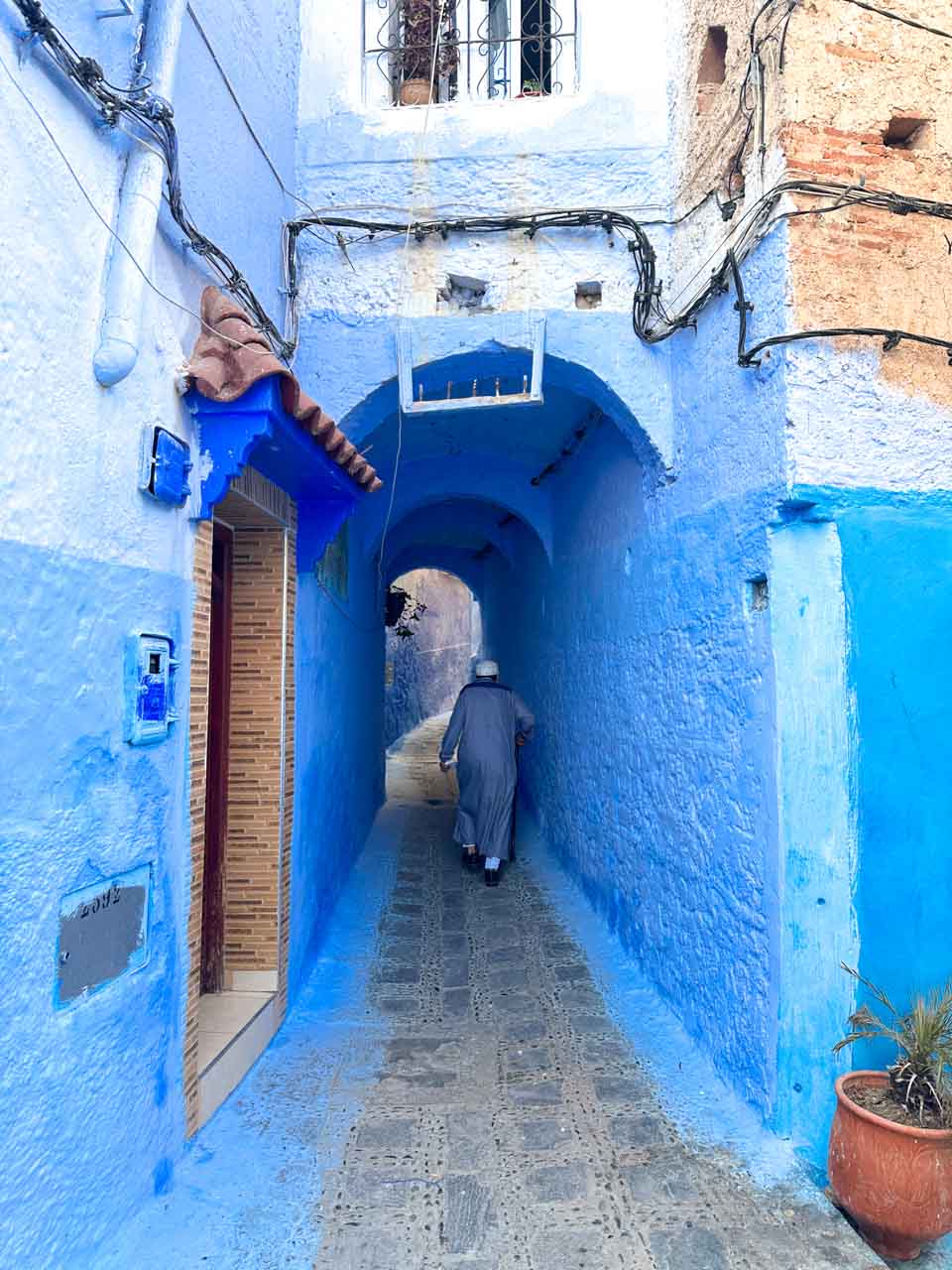 An elderly local walking down a blue alley beneath an arched passage in Chefchaouen, Morocco