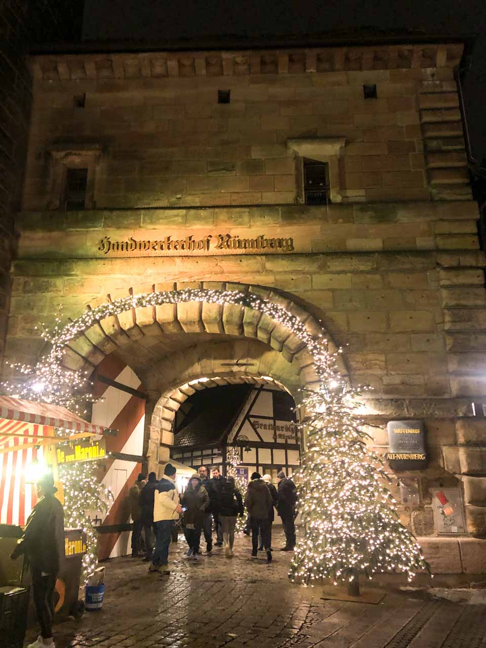A stone archway decorated with festive lights, leading into Handwerkerhof in Nuremberg, Germany, at night