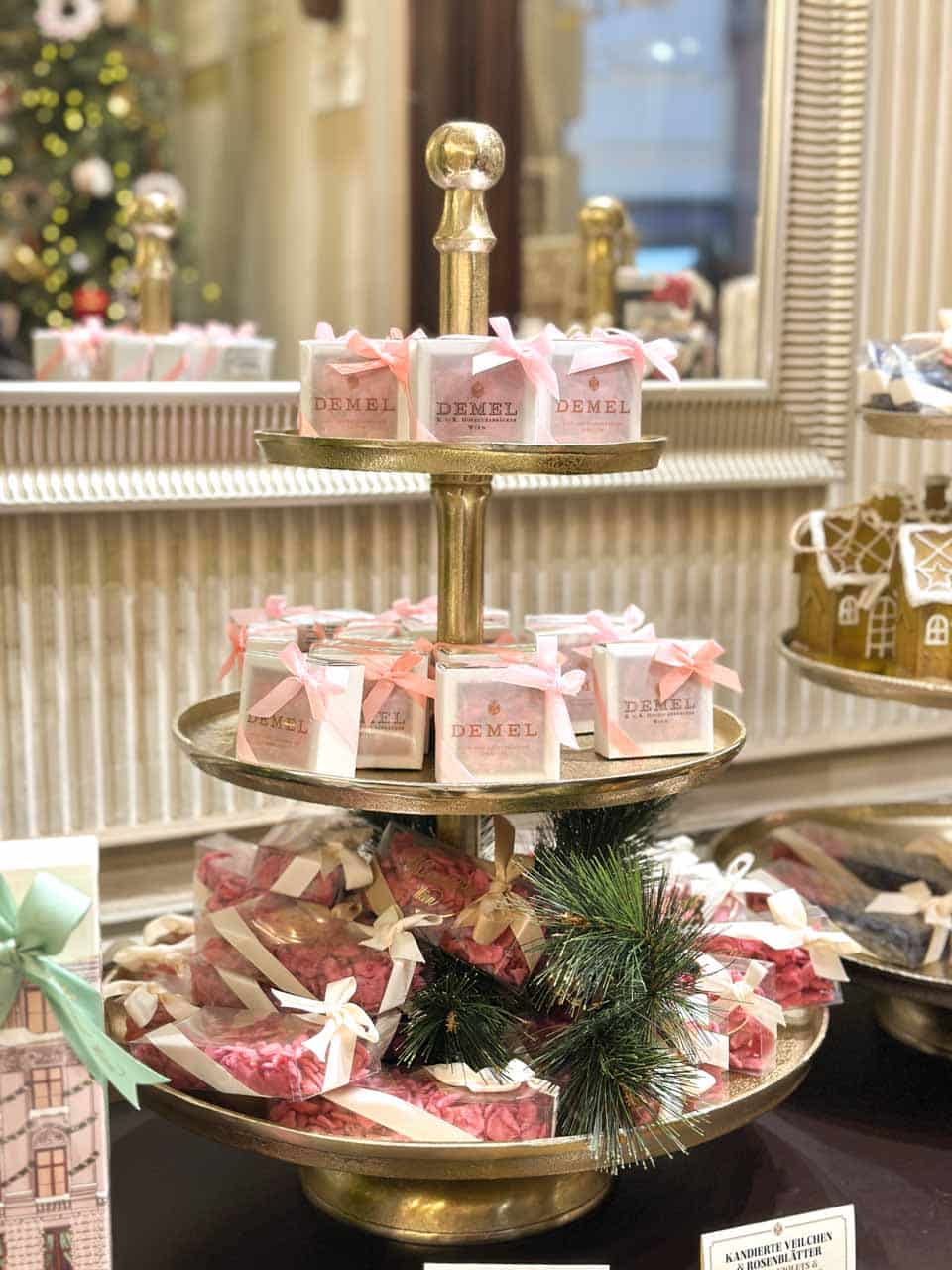 A tiered golden stand filled with beautifully wrapped Demel sweets, adorned with ribbons and pine branches