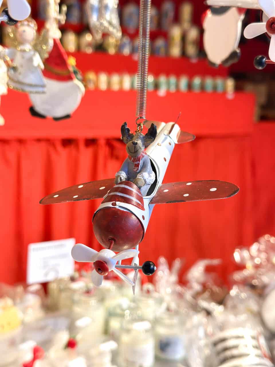 A festive Christmas ornament of a reindeer flying a red-and-white aeroplane, displayed at a market stall