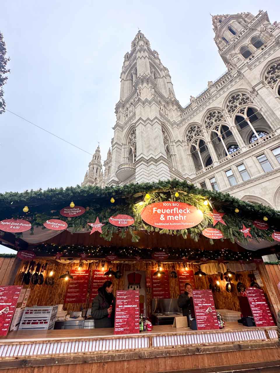 A vibrant Christmas market stall on Rathausplatz in Vienna selling traditional Austrian flatbreads, decorated with pine branches and festive lights