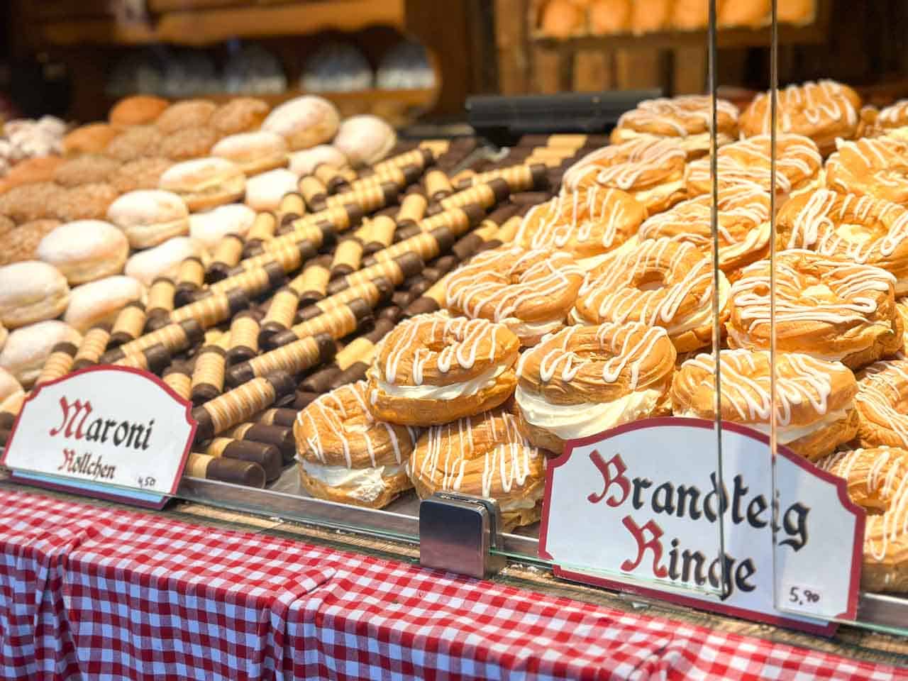Pastries and baked treats on display at a Christmas market stall in Vienna, including Brandteig rings topped with white icing