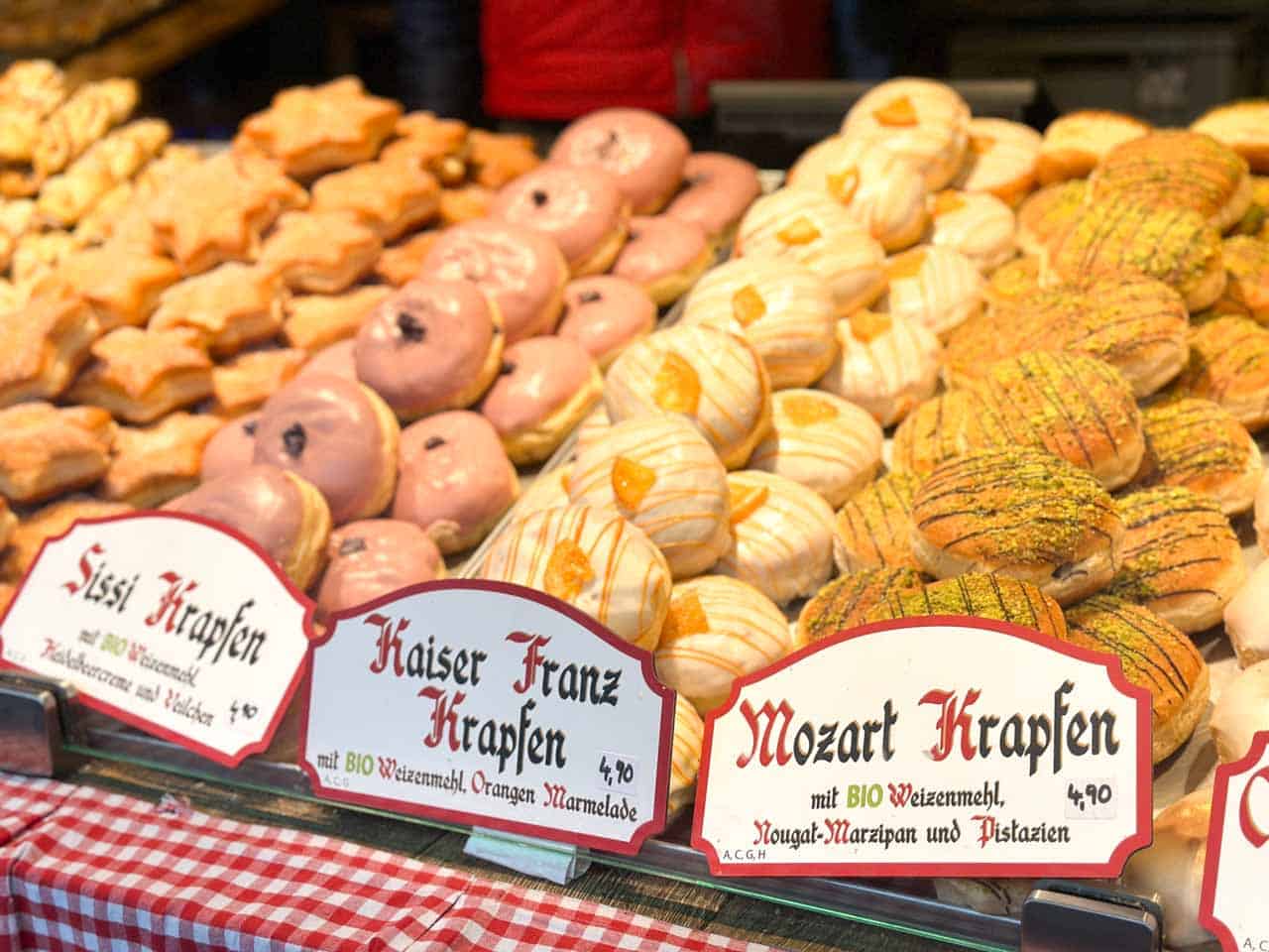 Rows of festive pastries, including Sisi, Kaiser Franz, and Mozart Krapfen, decorated with icing and nuts