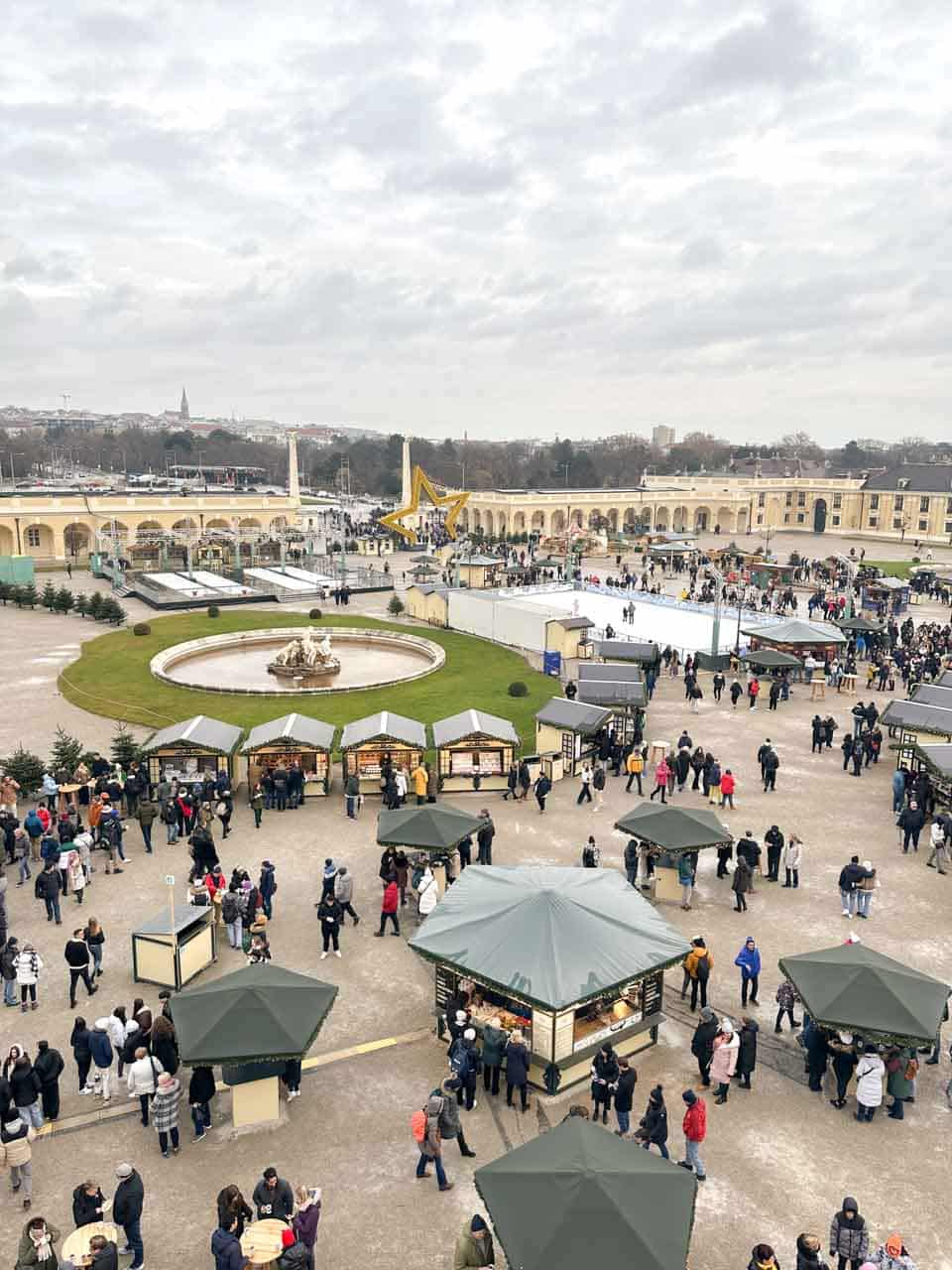 Aerial view of Schönbrunn Palace’s Christmas market with stalls, a fountain, and a large golden star installation