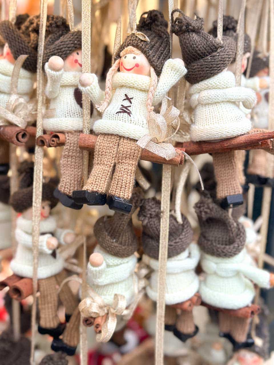 Handcrafted knitted ornaments of smiling girl dolls wearing cosy winter outfits, hanging from festive ribbons