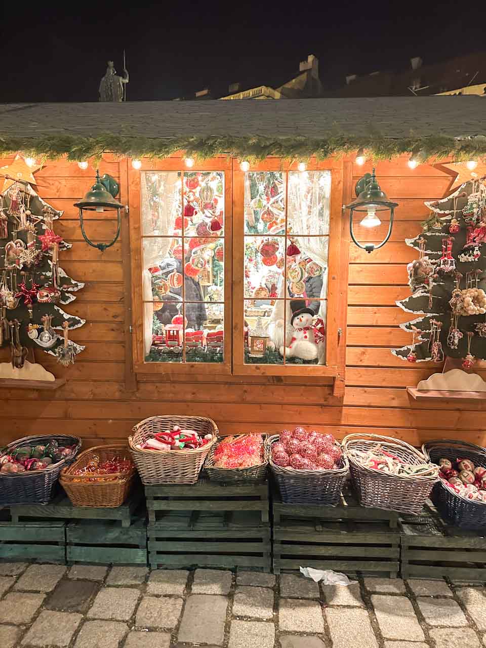 A cosy wooden stall at a Vienna Christmas market, decorated with lights and filled with baskets of colourful ornaments and festive decorations