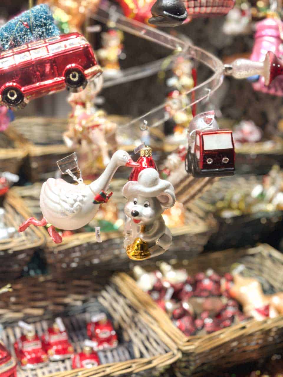 A close-up of colourful Christmas ornaments, including a goose and a mouse, displayed above wicker baskets at a Christmas market stall in Vienna