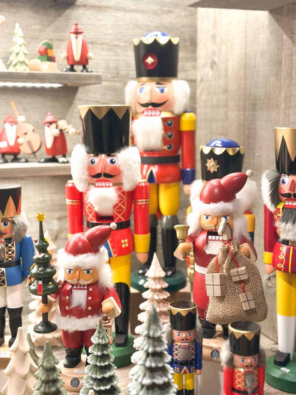 A festive display of traditional nutcrackers in bright red and gold, surrounded by small wooden Christmas trees and figurines