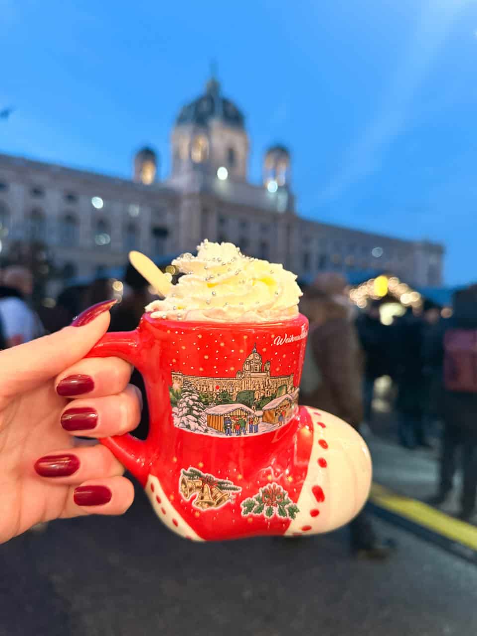 Woman holding up a festive mug shaped like a red boot, filled with whipped cream-topped punch