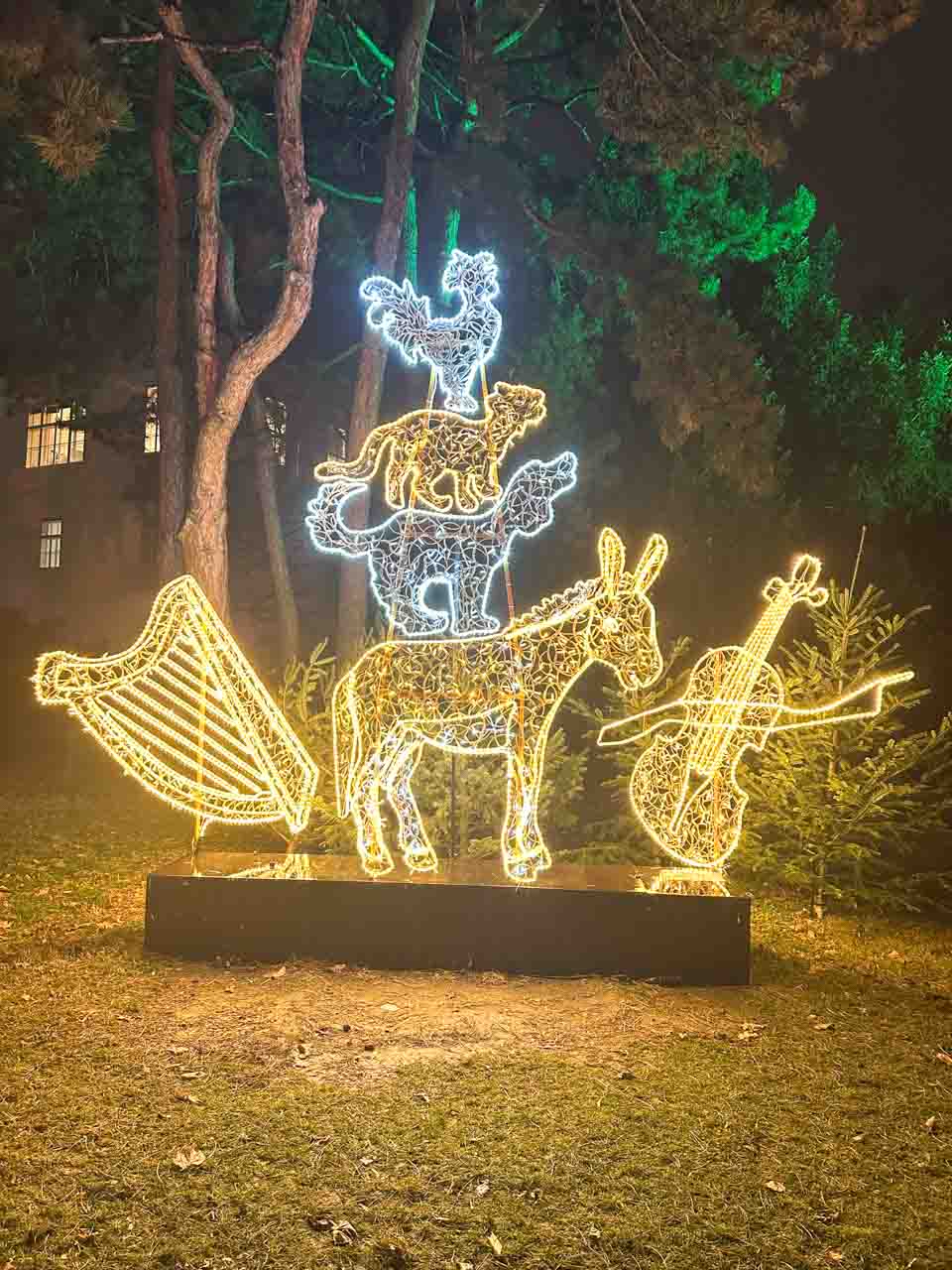 A light sculpture of the Town Musicians of Bremen, surrounded by trees with soft green lighting in the background