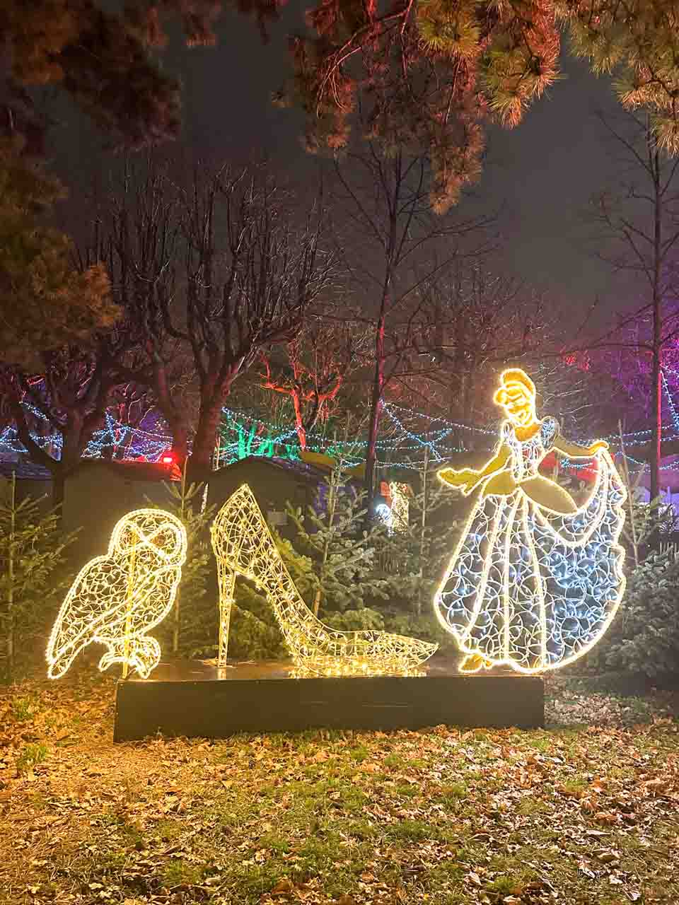 A glowing light sculpture featuring Cinderella, a glass slipper, and an owl surrounded by festive lights and trees