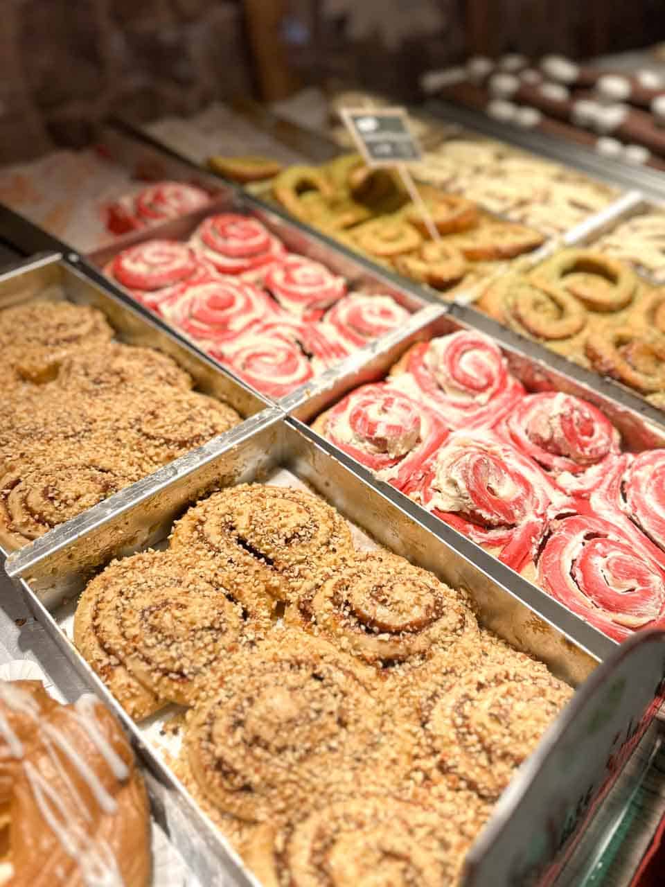Rows of sweet pastries, including cinnamon rolls and colourful swirl buns, displayed in trays at a Christmas market stall