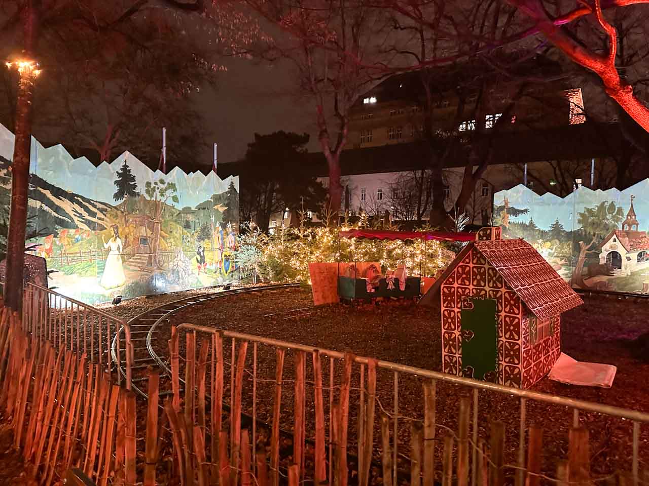 A small children’s train set with a gingerbread house and fairy lights, surrounded by painted Christmas scenes at the Altes AKH Christmas market in Vienna